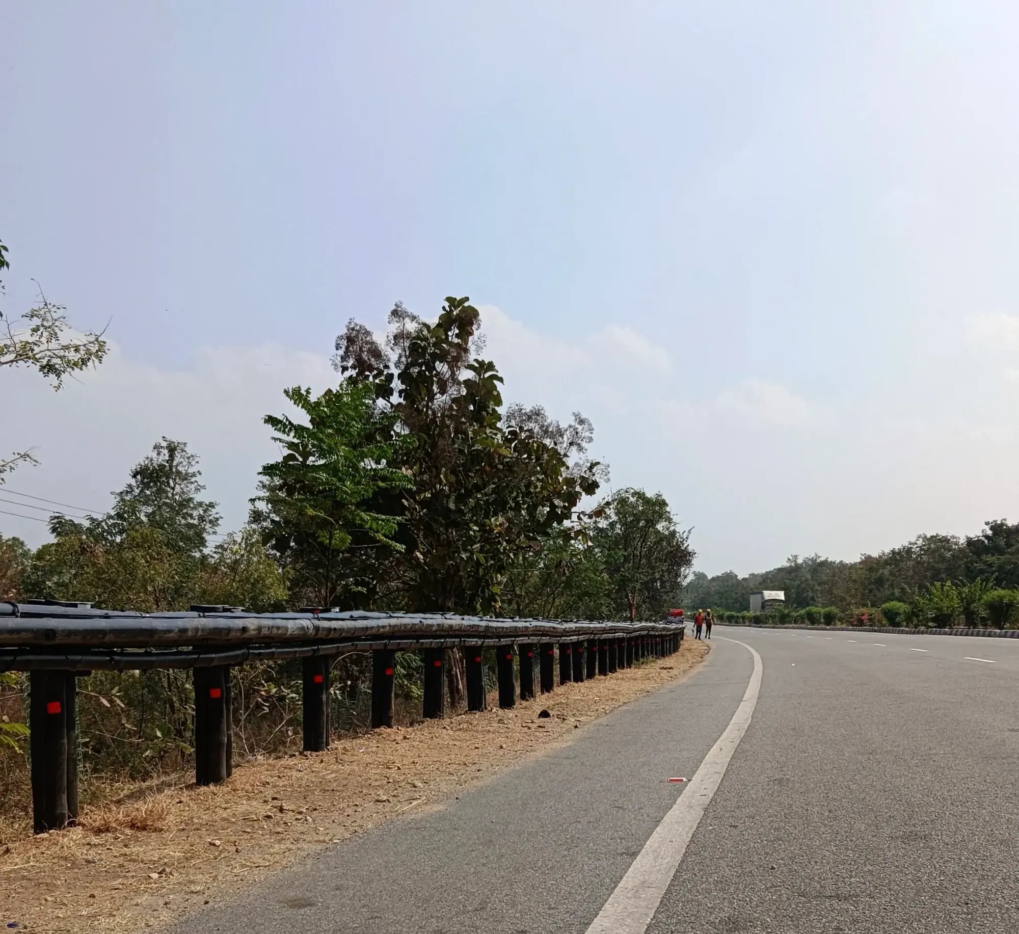 Kooch Kavach bamboo crash barrier installed along a curved highway with roadside trees